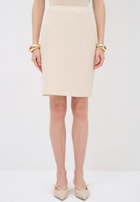 Falda de lápiz beige con un patrón texturizado, corte recto y cintura de altura media. Combinada con tacones nude de punta y una pulsera dorada en la muñeca.