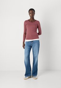 Maglietta a maniche lunghe, a righe bordeaux e rosa con scollatura rotonda, abbinata a jeans chiari a zampa d'elefante e sneaker con suola trasparente.