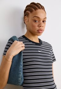 Ριγέ μαύρο και άσπρο μπλουζάκι με στρογγυλή λαιμόκοψη. Μια μπλε τζιν τσάντα κρατιέται στο αριστερό χέρι, με απαλό, υφασμάτινο φινίρισμα.