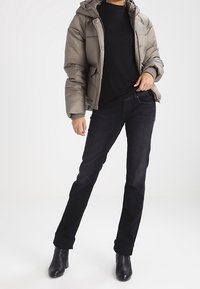 Puffjakke i dæmpet olivengrøn med hætte, parret med sorte tætsiddende jeans og ankelstøvler. Tekstureret stof, afslappet pasform og opsmøgede ærmer.