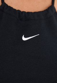 Black sleeveless top with gathered neckline. Features a white Nike logo stitched on the front, made from soft, stretchy fabric.