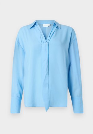 Gai zils ilgs piedurknis blūze ar apkakli un priekšējo auklu detaļu, izgatavota no gludas auduma, attēlota uz balta fona.