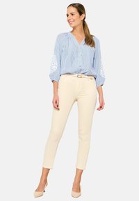 Blusa a rayas azul y blanca con mangas abullonadas, detalles bordados y botones en la parte delantera, combinada con pantalones crema ajustados y tacones nude.