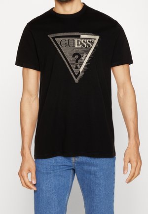 Schwarzes Baumwoll-T-Shirt mit einem silbernen dreieckigen Logo, das "GUESS" und ein Fragezeichen zeigt, rundem Ausschnitt und kurzen Ärmeln.