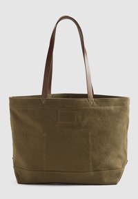 Sac fourre-tout en toile vert olive avec des poignées en cuir marron, forme rectangulaire, texture robuste et un petit détail d'étiquette sur le côté.