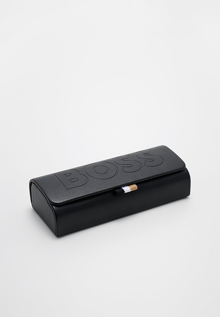 Étui à lunettes rectangulaire noir avec logo 'BOSS' en relief, texture lisse, fermeture magnétique et petite rayure décorative en or, blanc et noir.