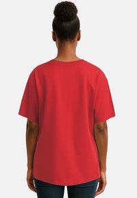 T-shirt di cotone rosso con maniche corte, scollo rotondo e vestibilità ampia. Il tessuto appare liscio, senza motivi o dettagli visibili.