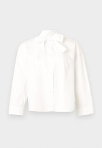 Λευκό μακρυμάνικο πουκάμισο με κουμπιά και μεγάλο φιόγκο δεμένο στο λαιμό, παρουσιασμένο σε μια επίπεδη, ουδέτερη επιφάνεια.