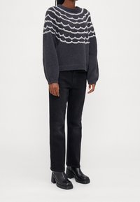 Szary sweter dzianinowy z białym falistym wzorem; luźny krój, ściągacze na mankietach, w zestawie z czarnymi dżinsami prostymi i czarnymi botkami na obcasie.