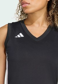 Top deportivo negro sin mangas con diseño de escote en V, que presenta el logo blanco de Adidas en el hombro izquierdo y paneles laterales en contraste. Textura de tela suave.