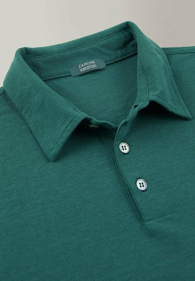 Polo shirt verde scuro in cotone, con colletto classico, patta con tre bottoni e una texture morbida e liscia. Etichetta del marchio visibile.