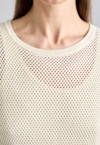 Maglione in maglia leggera con design a rete, colletto rotondo e motivo testurizzato, che lascia intravedere la pelle sottostante.