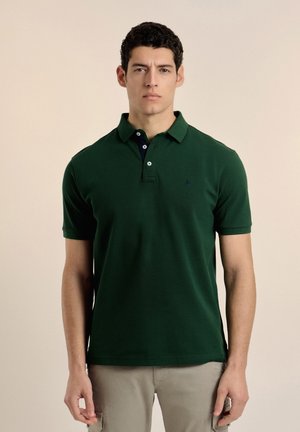 Polo de color verde oscuro con cuello clásico, tapeta de dos botones y logo sutil. Mangas cortas y una textura de algodón suave.