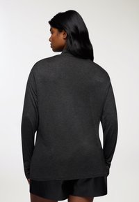 Czarna koszula z długim rękawem, okrągłym dekoltem, luźny krój i miękka tkanina. Gładka faktura i delikatny połysk, noszona na ciemnych szortach.