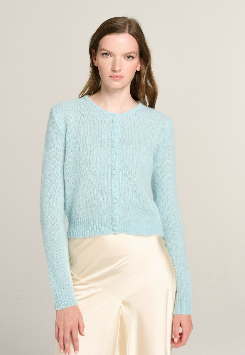 Light blue cropped cardigan made of soft, textured fabric with a round neckline, long sleeves, and button closures down the front.