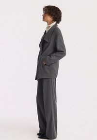 Szary wełniany płaszcz z szerokim kołnierzem, bocznymi kieszeniami i luźnym krojem, połączony z szerokimi szarymi spodniami. Gładka tekstura i minimalistyczny design.