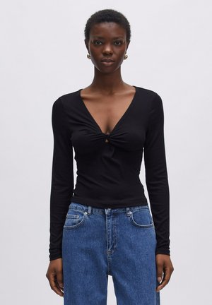 Zwarte lange mouwen top met een V-hals en een twistdetail op de borst. Strakke pasvorm met geribbelde textuur, gecombineerd met hoge, blauwe jeans.