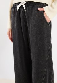 Zwarte, zachte stoffen broek met wijde pijpen en een elastische tailleband, voorzien van een trekkoord en zijzakken, getoond op heuphoogte.