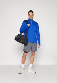 Blå langærmet zip-top med en brystlomme, grå shorts og beige træningssko. Sort træningstaske med skulderrem.