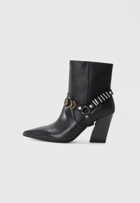 Bottines noires en cuir avec bout pointu, talon empilé et sangle décorative avec quincaillerie métallique et clous. Texture lisse.