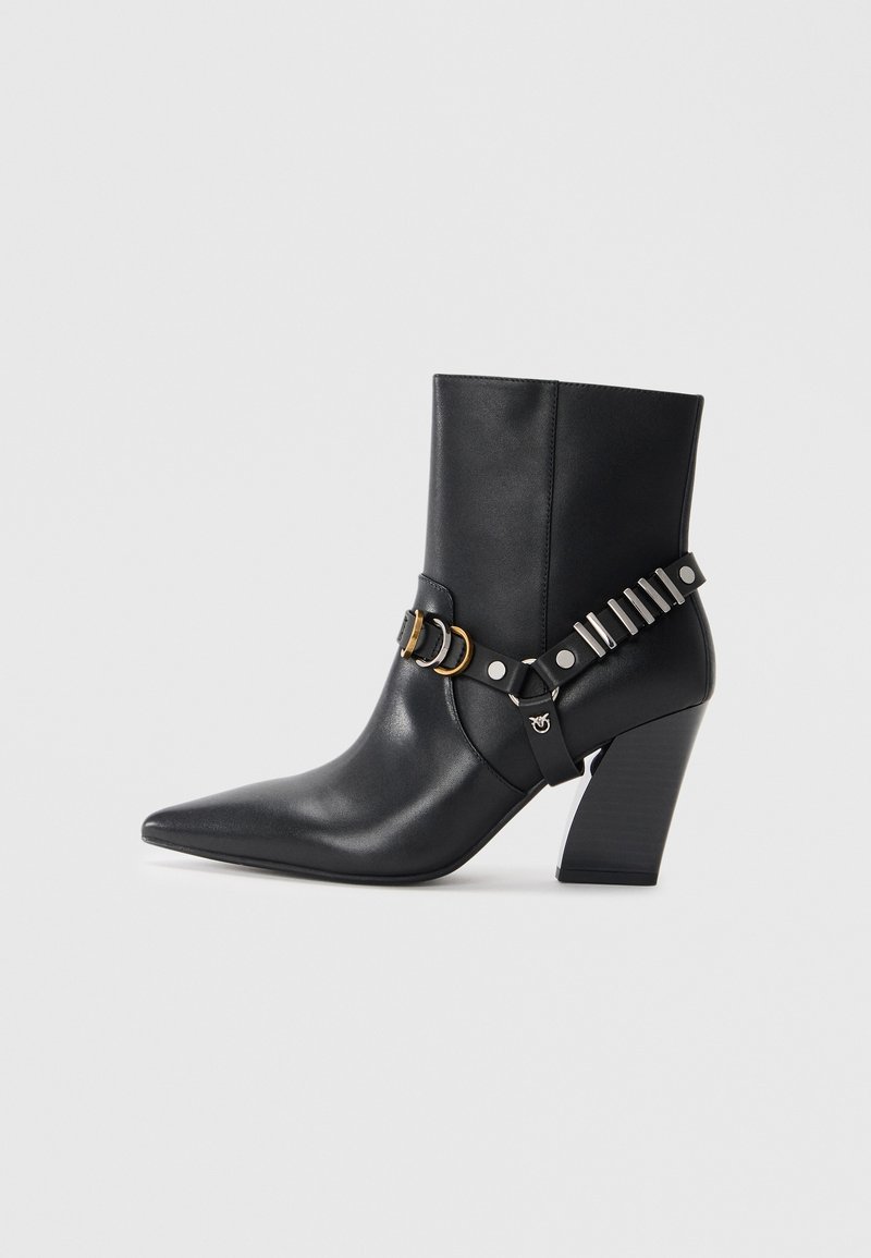 Bottines noires en cuir avec bout pointu, talon empilé et sangle décorative avec quincaillerie métallique et clous. Texture lisse.