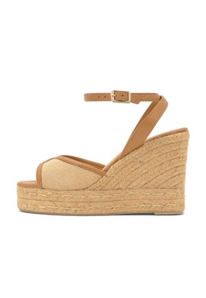 Sandalo con zeppa color cuoio con piattaforma in juta intrecciata, punta aperta e cinturino alla caviglia con fibbia dorata su sfondo bianco.