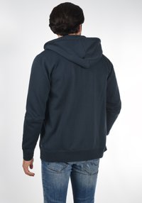 Marineblauer Hoodie aus weichem Stoff, mit Kordelzug-Kapuze und gerippten Bündchen, getragen mit hellblauen Jeans.