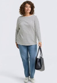 Langærmet top med striber i sort og hvid, kombineret med lyseblå jeans. Model holder en sort håndtaske og har hvide sneakers på.