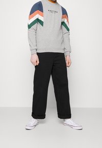 Gray sweatshirt with multicolored chevron stripes in blue, orange, and green, paired with black wide-leg pants and white sneakers.