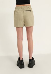 Shorts beiges avec une ceinture élastique, une poche zippée à l'arrière, et une coupe décontractée, associés à des baskets chunky noires.