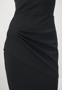 Robe noire au design ajusté avec un tissu doux et extensible. Un détail plissé notable crée de la texture et un intérêt visuel sur le côté.