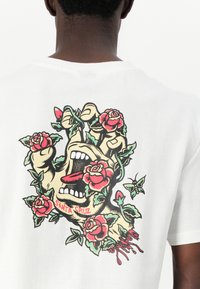 White cotton t-shirt featuring a colorful graphic of a hand with a face surrounded by roses, displaying red, green, and black details.
