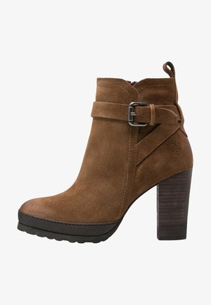 Brown suede ankle boot with a chunky heel, featuring a decorative strap and buckle detail, rounded toe, and textured wooden heel.