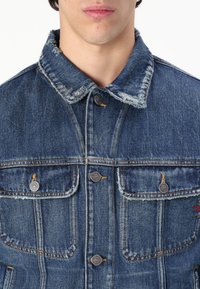 Denim jacket with a faded blue color, structured collar, and four front pockets. Features metal buttons and visible stitching details.