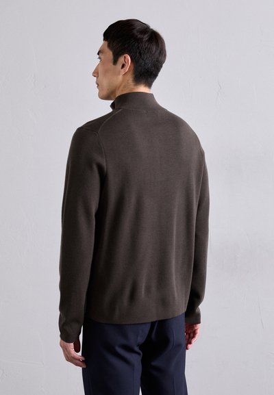 Maglione attillato di colore marrone scuro con colletto alla coreana, maniche lunghe e tessuto sottile. Dettaglio discreto della cucitura sulla spalla, visto da dietro.