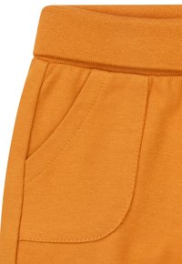 Oranger Baumwollstoff, der einen Taillenbund und eine seitliche Tasche mit sichtbaren Steppnähten und Struktur zeigt. Einfaches Design mit weicher Verarbeitung.