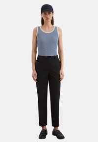 Gestreept tanktop in blauw en wit, gecombineerd met op maat gemaakte zwarte broeken. Model draagt een marineblauwe pet en zwarte instappers. Eenvoudig, modern ontwerp.