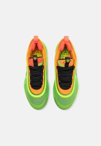 Kleurige sportschoenen hebben een groene mesh bovenkant, zwarte veters en oranje accenten. De tong heeft een grafisch ontwerp in oranje en groen.