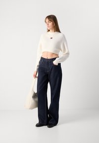 Crop sweater in cream knit, high-waisted dark denim pants, and black slip-on shoes, complemented by a light beige shoulder bag.
