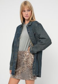 Džínová oversized bunda, šedé tričko s kruhovým výstrihom a mini sukňa s flitrami v leopardom vzore. Bunda má gombíkové zapínanie a dve vrecká.