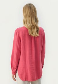 Langærmet, knappet skjorte i intens pink. Lavet af letvægtsstof, med en buet kant og sideslids for bedre bevægelsesfrihed.