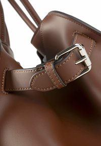Bruine leren handtas met een zilveren metalen gesp, contrasterende stiksels en een gladde textuur met een gestructureerd ontwerp.