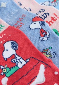 Four pairs of knitted socks featuring Snoopy. Colors include red, blue, and pink. Patterns depict Snoopy in festive scenes with details like snowflakes.