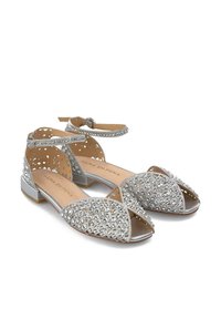 Chaussures ouvertes en argent décorées de strass, avec un design découpé et des brides pour la cheville. Semelle plate avec un accent métallique.