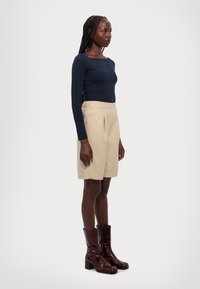 Marinblå langermet topp, beige plissert shorts med elastisk midje, og blanke burgunder knehøye støvler med tykt hæl.