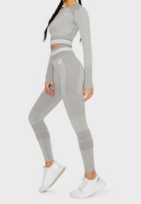 Grauer sportlicher Croptop und Leggings mit strukturierten Mustern, die einen hohen Bund und weiße Akzente aufweisen, kombiniert mit weißen Sneakers.