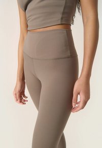 Világosbarna sportleggings, magas derékkal, varrás nélküli kialakítással és finom varrási részletekkel, párosítva egy megfeleő vágott toppal.