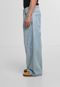 Hellblaue, weit geschnittene Jeans aus Denim mit kontrastierenden Nähten und hoher Taille. Mit einem vorderen Knopfverschluss und zwei Gesäßtaschen.