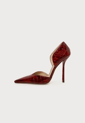 Chaussure à talon haut rouge avec bout pointu, texture crocodile, design ouvert sur le côté et talon aiguille sur un fond clair uni.