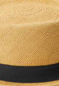 Olkihattu, jossa on kudottu rakenne, vaaleanruskea väri ja musta grosgrain-nauha pohjan ympärillä. Pyöreä kuvio hatussa.